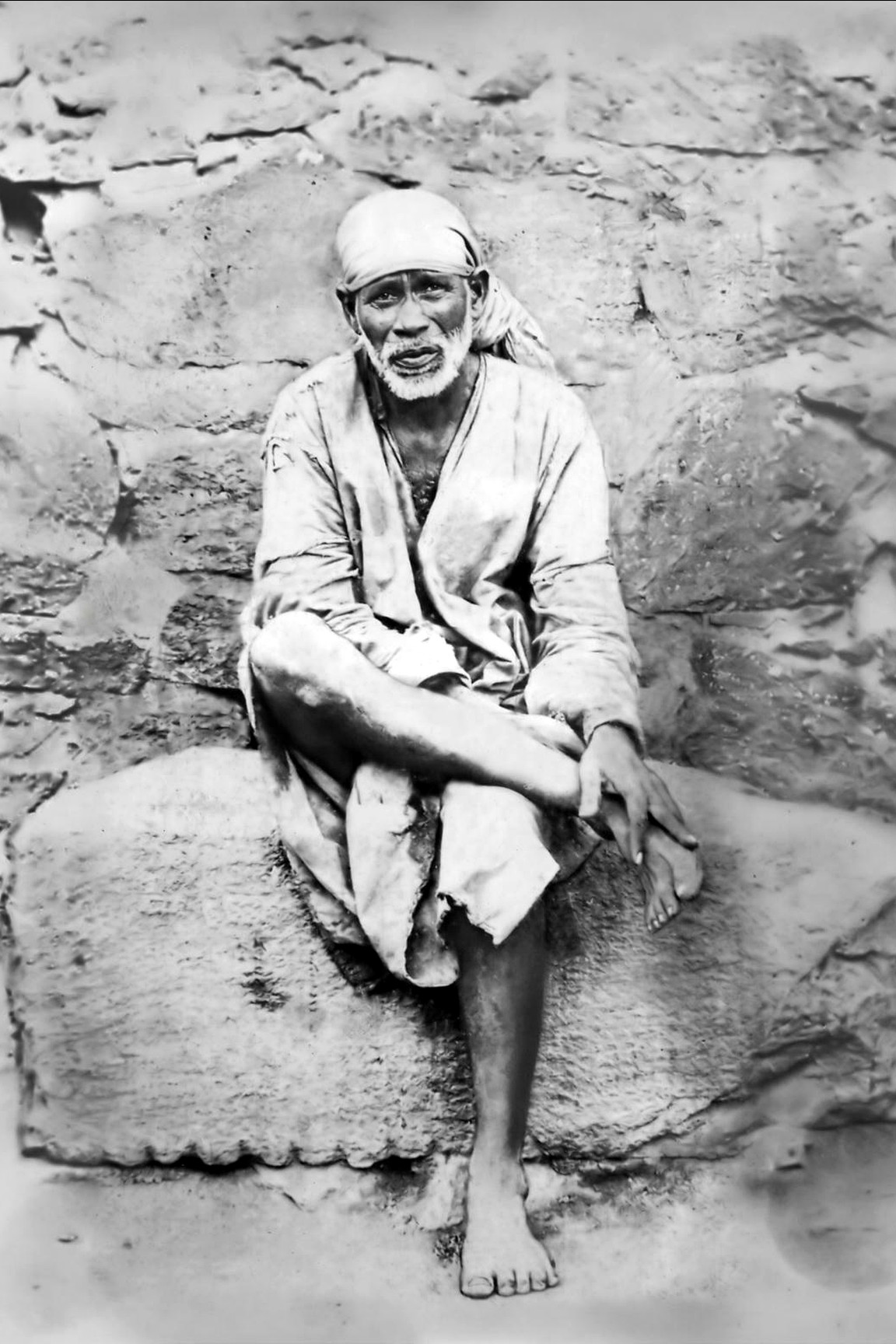 Original public-domain photograph of Shirdi Sai Baba sitting on a stone, taken in his lifetime